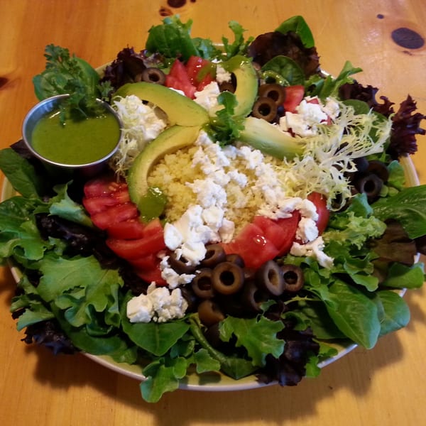A vibrant Fudenjuce healthy salad with greens, tomatoes, olives, avocado, feta, and green dressing.