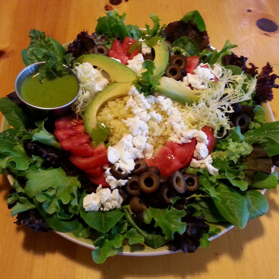 A vibrant Fudenjuce healthy salad with greens, tomatoes, olives, avocado, feta, and green dressing.