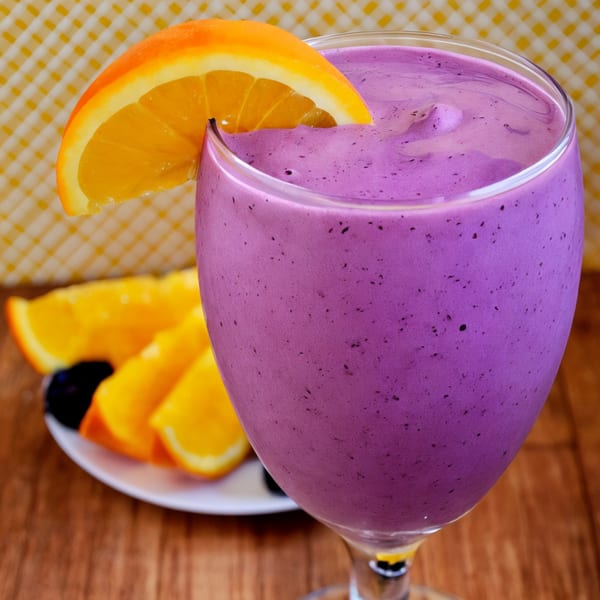 A vibrant purple Fudenjuce smoothie in a glass, garnished with a fresh orange slice.