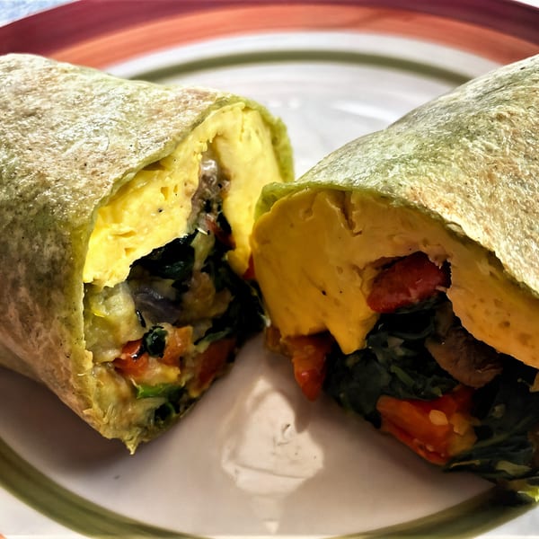 A healthy Fudenjuce breakfast burrito, cut in half, revealing scrambled eggs and colorful vegetables.
