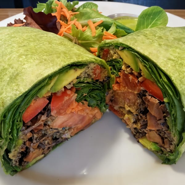 A Fudenjuce healthy wrap, cut in half, revealing fresh vegetables and a side salad.