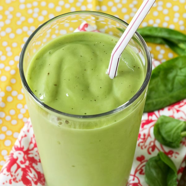 A vibrant green Fudenjuce smoothie in a glass with a straw, surrounded by spinach leaves.