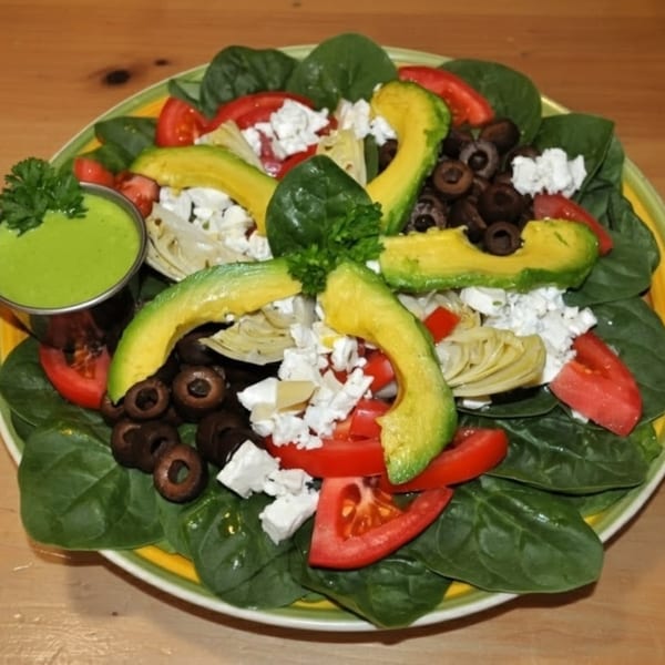 A vibrant Fudenjuce salad with spinach, avocado, tomatoes, olives, feta, and green dressing.