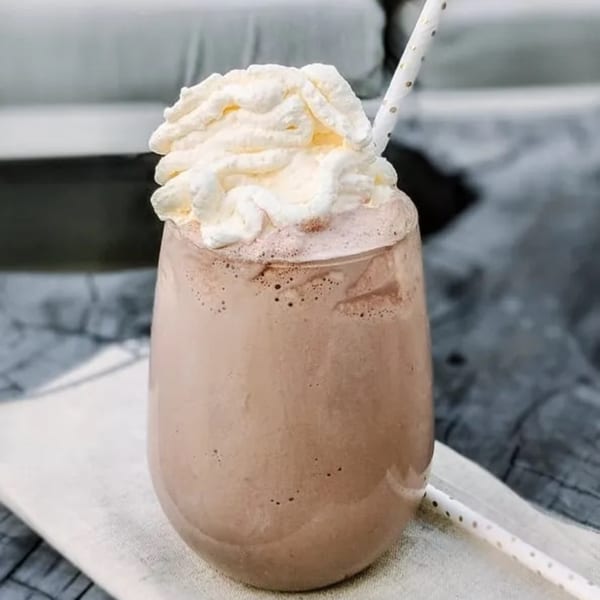 Fudenjuce's chocolate milkshake with whipped cream and a polka-dotted straw on a wooden table.